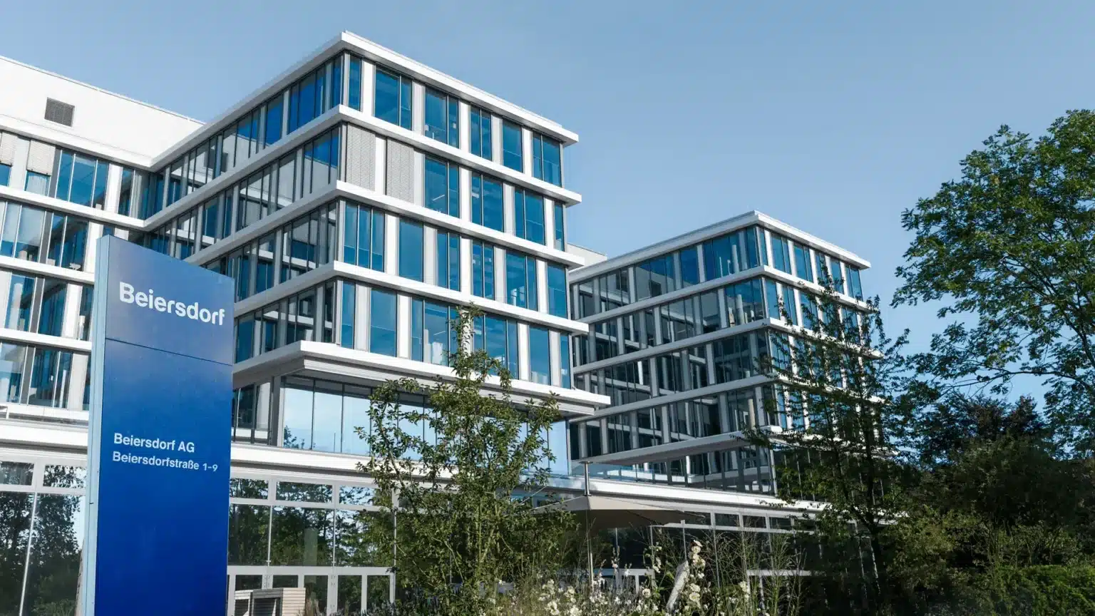 Modern office building with large glass windows and a sign reading "Beiersdorf" in front. Trees and greenery are visible around the building, with efficient parking lot management facilitated by Wayleadr ensuring smooth parking operations for all employees and visitors.