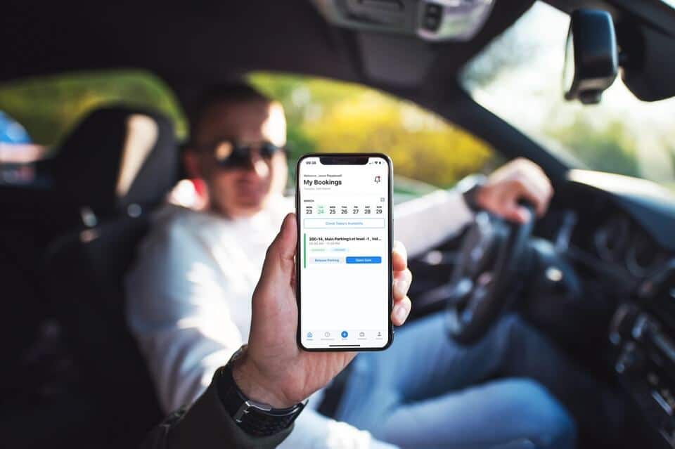 Person sitting in a car while holding a smartphone with a parking management app displayed on the screen.