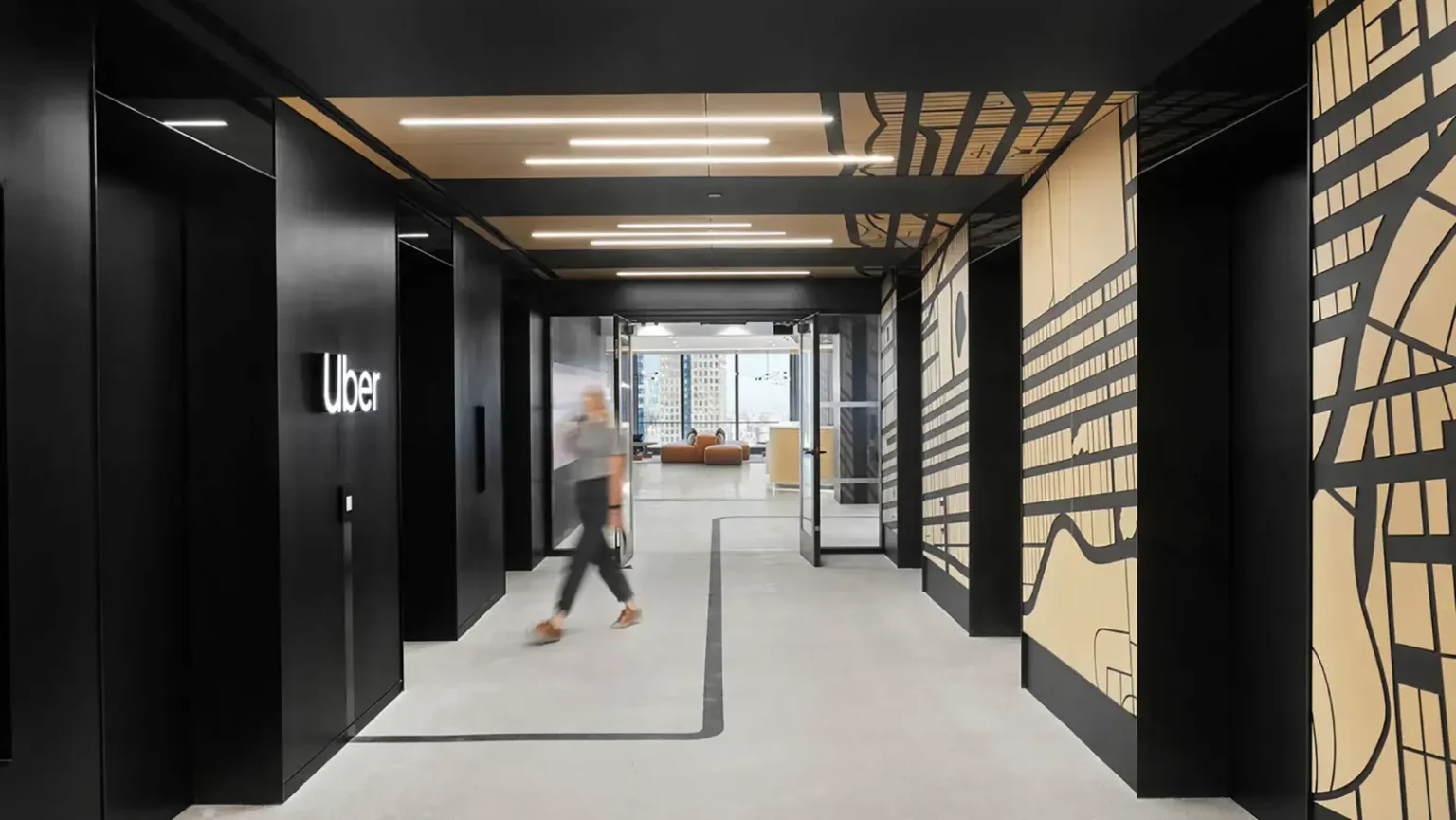 A person walks through a modern office hallway with black and beige walls featuring graphic designs. The Uber logo is visible on the left wall, hinting at advanced solutions like Wayleadr for visitor parking and efficient parking lot systems.