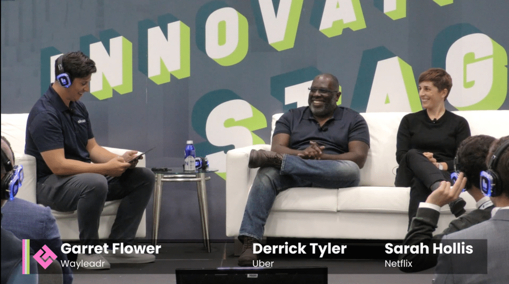 Three people are seated on stage with a backdrop reading "INNOVATE STAGE." The screen identifies them as Garret Flower from Wayleadr, focusing on parking management, Derrick Tyler from Uber, and Sarah Hollis from Netflix.