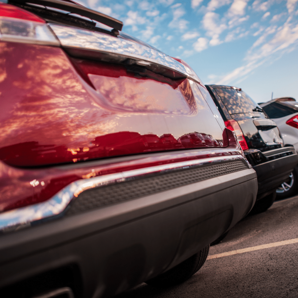 Close-up of the rear of three parked cars at sunset, highlighting their bumpers and tailgates in a well-organized commercial parking area.