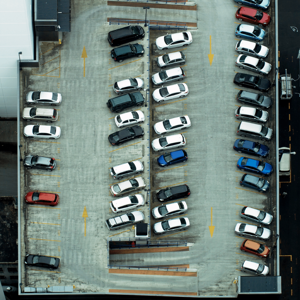 Aerial view of a commercial parking garage with multiple rows of parked cars, many in black, white, and various other colors, arranged in organized rows and columns. Wayleadr's parking lot management system ensures seamless organization and efficiency.