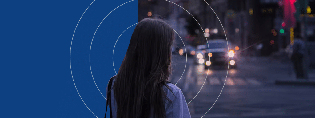 A person with long hair is standing on a city street at dusk, looking at oncoming headlights. Circular blue graphic overlays partially cover the left side of the image, highlighting the efficient commercial parking systems in place nearby.