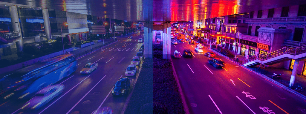 A city street scene at night, split into two halves with different color tones: the left side in blue hues, and the right side in red and purple hues, with busy traffic, commercial parking areas, and illuminated buildings.