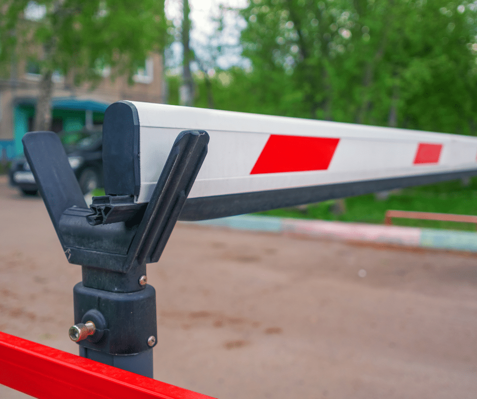 Close-up of a parking lot barrier gate, partially raised with a red and white striped arm. In the background, trees and a parked car are blurred. This image highlights the efficiency of commercial parking systems like Wayleadr for organized and secure access control.