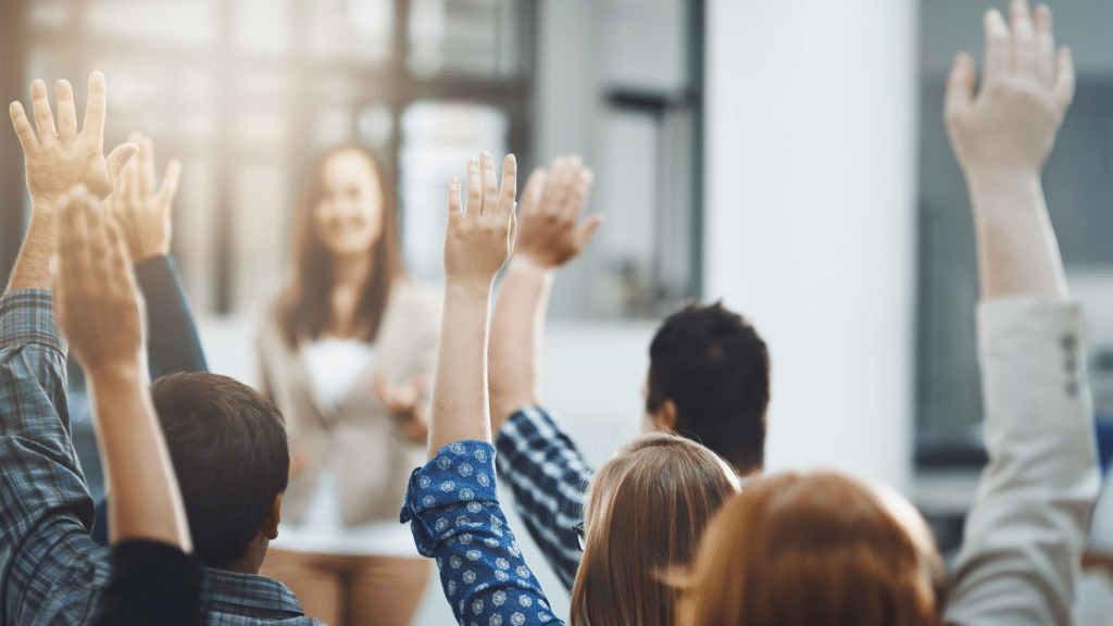 Group of people seated with their hands raised, facing a person standing at the front of a bright, modern room discussing visitor parking.