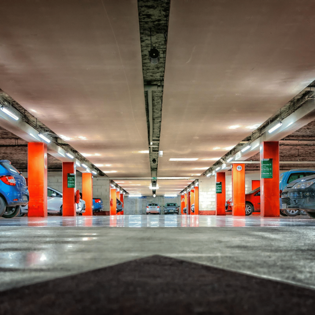 A brightly lit underground parking garage with numerous orange pillars, parked cars on both sides, and a polished concrete floor showcases efficient parking lot systems.