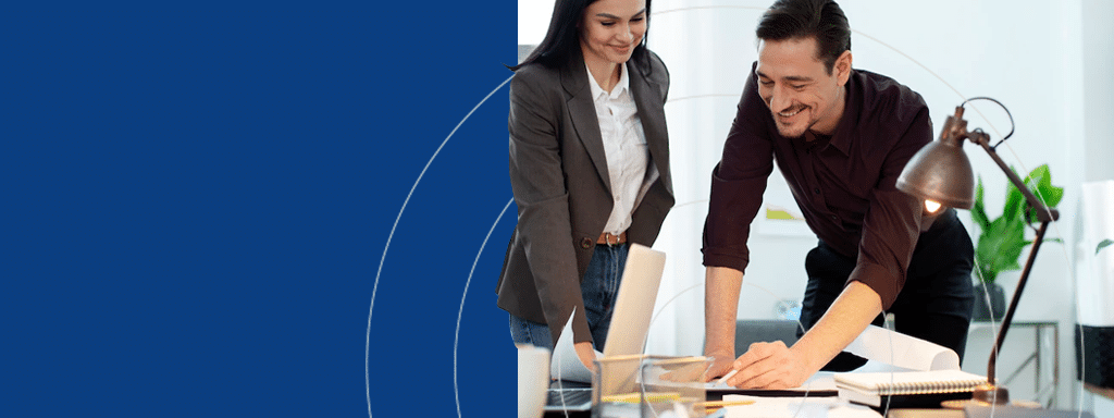Two people working together at a desk, one standing and the other leaning over. They are looking at documents and a laptop, discussing parking lot management. Office supplies and a lamp are on the desk. Blue background on the left.