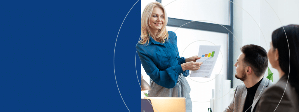 A woman in a blue blouse stands and holds a chart, presenting to two seated individuals in a professional setting, discussing commercial parking solutions.