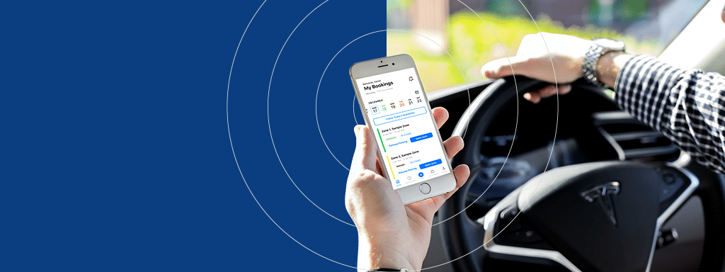 A person holds a smartphone displaying the "My Bookings" screen while steering a Tesla car, highlighting how Wayleadr seamlessly integrates technology in vehicles for efficient commercial parking.