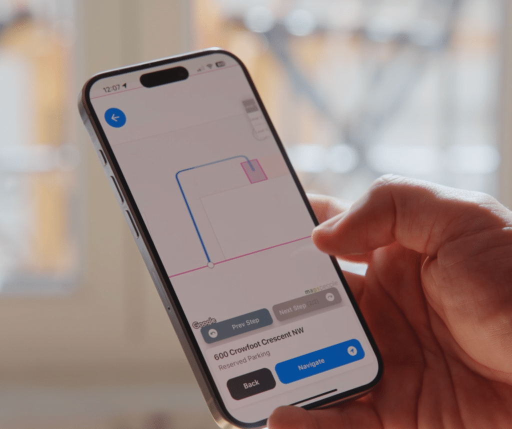 A hand is holding a smartphone with a navigation app open, displaying a route and the address "600 Crowfoot Crescent NW." The app also highlights visitor parking options nearby, ensuring seamless navigation for anyone heading to the location.
