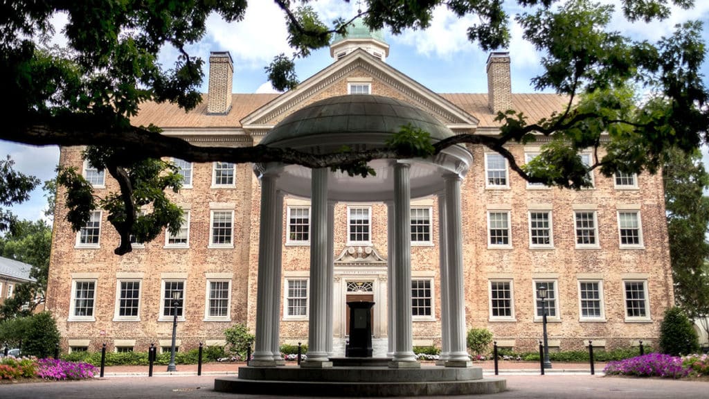 A classical architectural structure with columns stands in front of a large brick building with numerous windows, seamlessly integrating commercial parking solutions. Trees frame the scene.