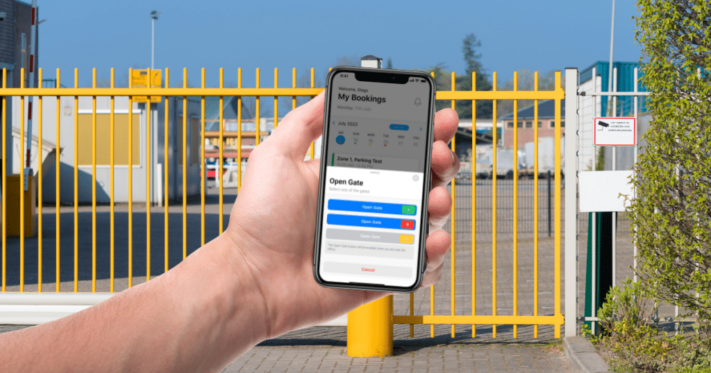A hand holds a smartphone displaying a gate control application in front of a yellow gate and industrial area, showcasing parking lot management features.
