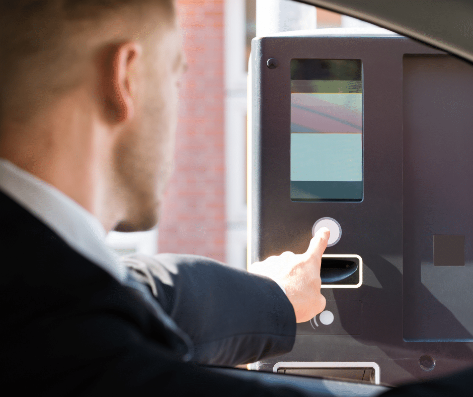 A person in a car presses a button on a drive-thru kiosk, seamlessly integrated with advanced parking lot management technologies.