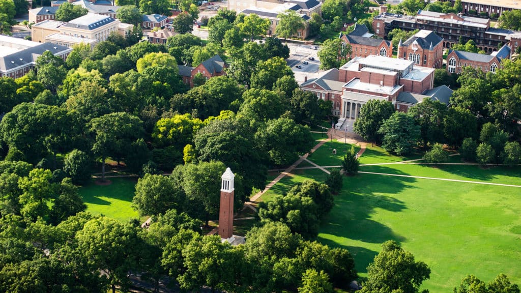 Aerial view of a university campus featuring a clock tower, several academic buildings, green spaces with trees and walkways, efficiently designed with Wayleadr's advanced parking lot management system.