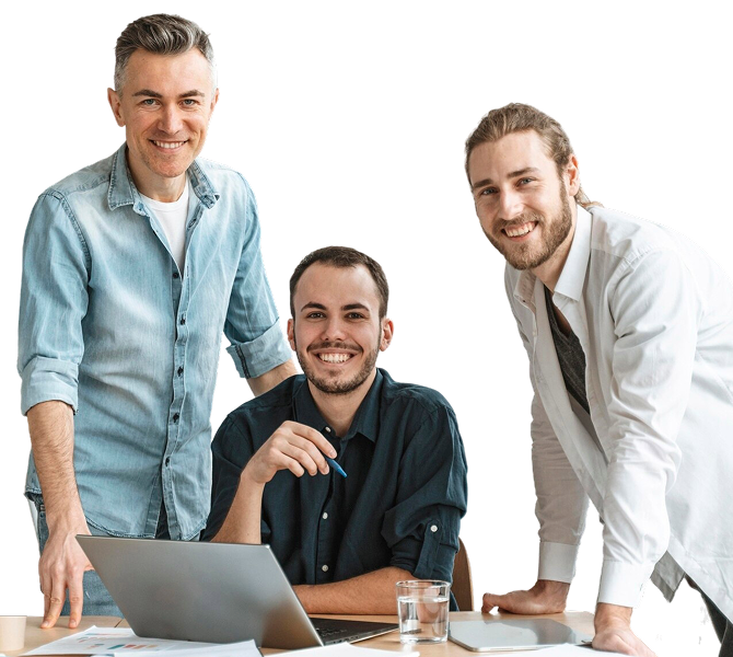 Three men smiling, gathered around a table with a laptop, documents, and a glass of water in a bright office setting.