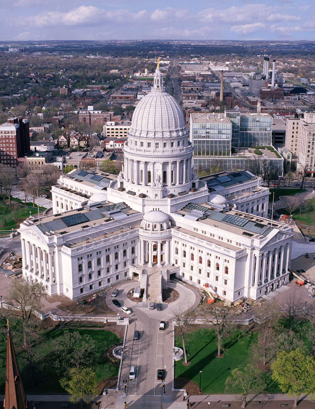 Aerial view of the Wisconsin DOA’s large white domed government building with four wings, surrounded by trees and a city landscape in the background.