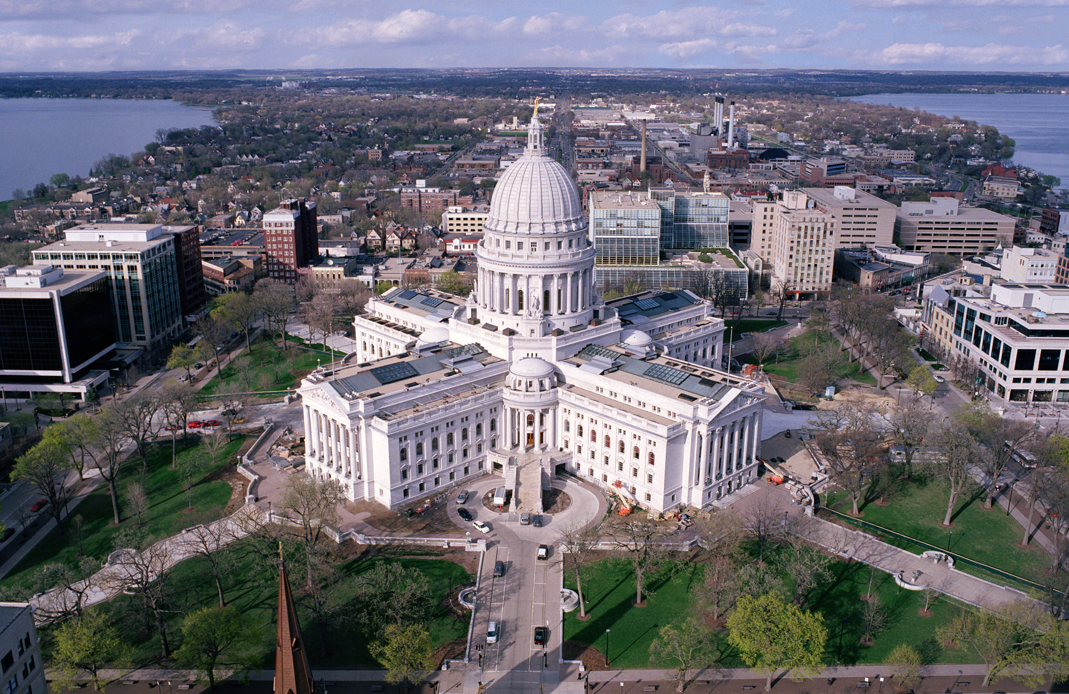 Aerial view of the Wisconsin State Capitol building in Madison, home to the Wisconsin DOA, surrounded by city buildings, trees, and nearby lakes.